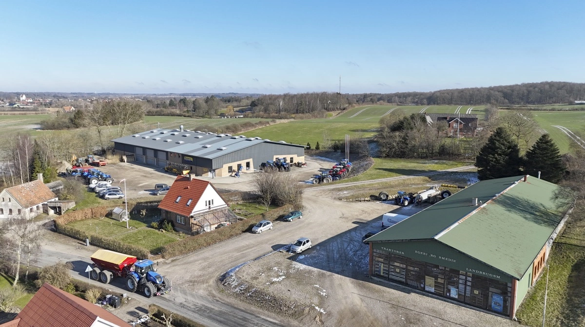 Midt i de sydfynske alper tæt ved Kirkeby har Egebjerg Smedie ligget siden 1700-tallet. På Alpevej passerer en New Holland-traktor fra den lokale maskinstation forbi maskinforretningen med den nyeste værksteds- og lagerbygning i baggrunden og til højre den hidtidige bygning, som indtil videre huser mejetærskerværkstedet og kontoret. Til venstre den oprindelige landsbysmedje. Fotos: Erik Hansen