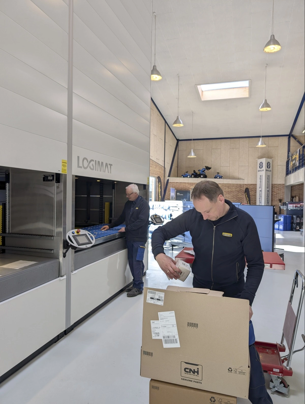 I den nye butiks- og lagerafdeling ses Bent Knudsen (i baggrunden) i færd med at betjene robot-højlageret med New Holland-reservedele og Anders Christoffersen med udpakning af reservedele.