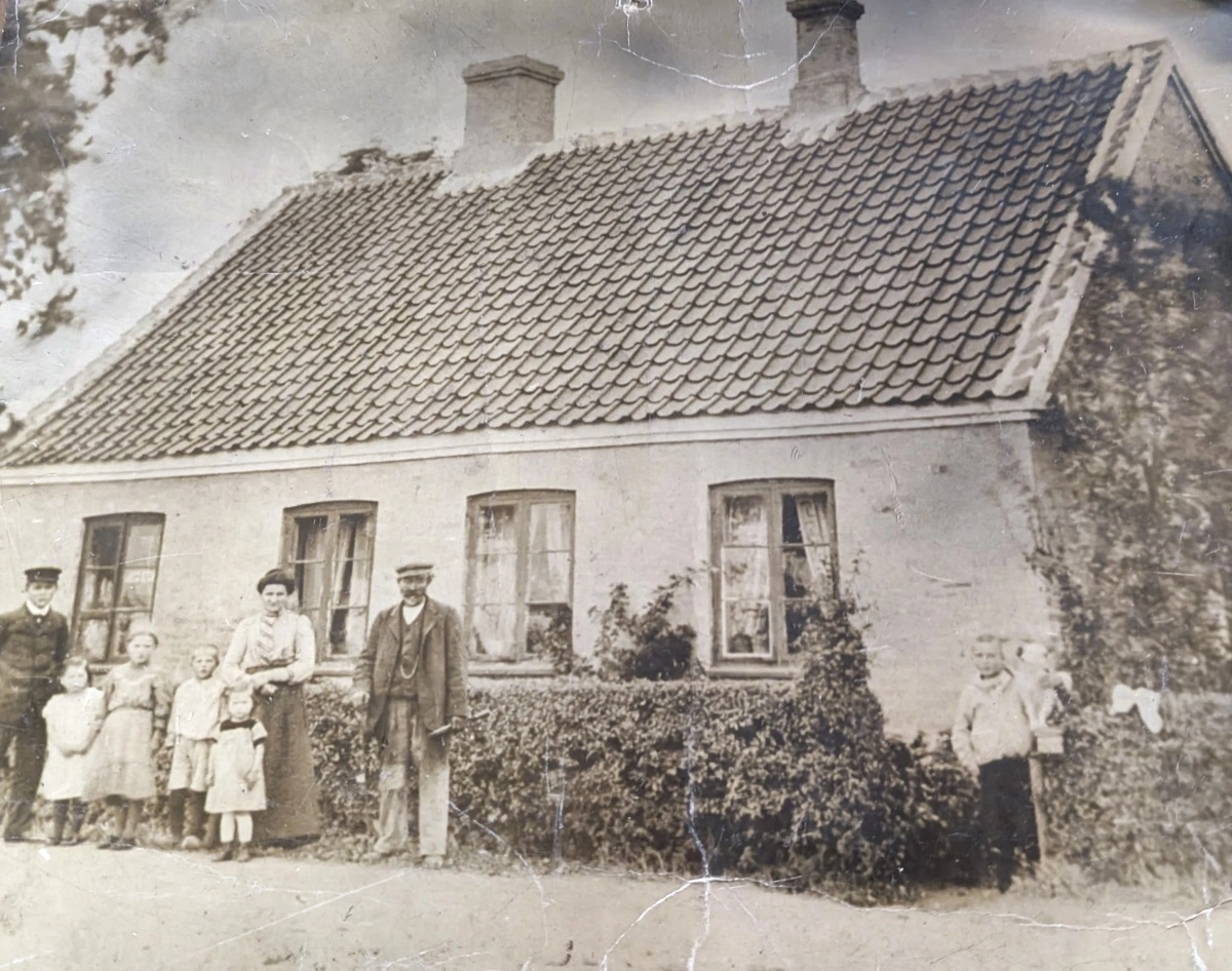 Landsbysmedjen i Frøslev startede i 1900 i dette nybygede hus. Karen og Per Andersen og deres 12 børn boede i den anden halvdel af huset. Til venstre for sin mor er det sønnen Bengt, der senere førte smedjen videre med produktion af stubharver og Ferguson transportkasser.