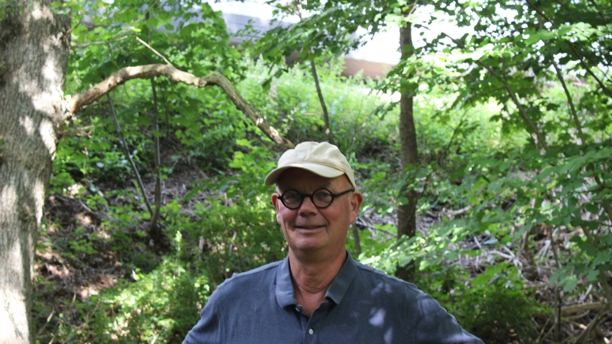 Skovejer Andreas Hastrup, Avnsøgård, er en af de lodsejere, der føler sig i klemme som følge af elektrificering af jernbanestrækningen Holbæk-Kalundborg. Han står i sin Natura-2000-skov, hvor det anes, at toget farer forbi i baggrunden. Han forklarer, at risiko for krav om erstatning tvinger ham til at fælde træer, han ellers gerne ville bevare, og han er ked af, at det får konsekvenser for naturen. Foto: Anne Wolfenberg
