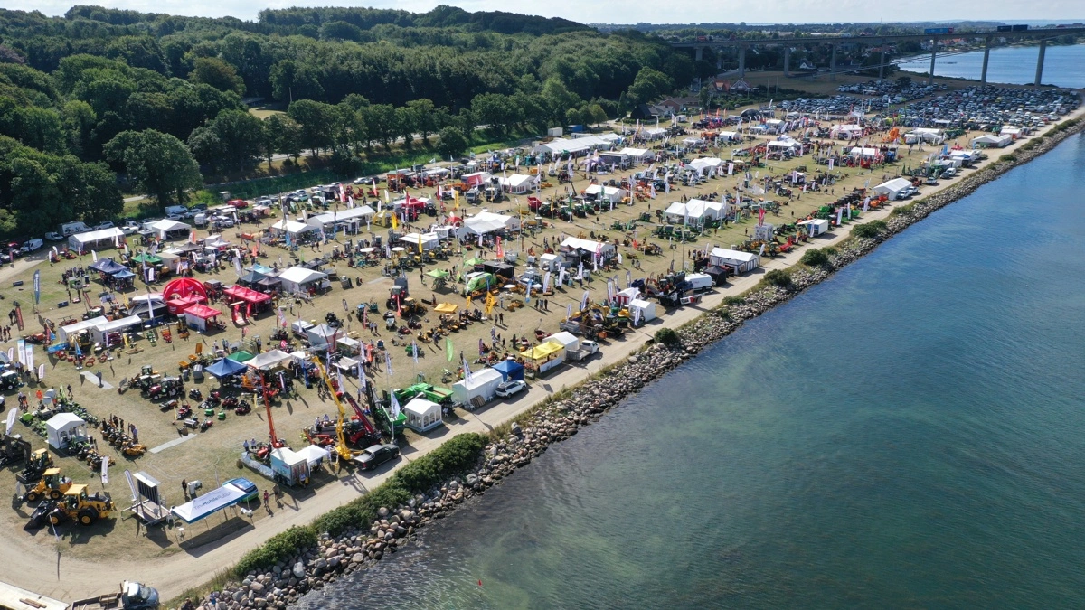 Set fra luften breder Maskiner under Broen sig langs Lillebælt med stande, specialmaskiner og besøgende helt ud til vandkanten. Dronefotoet er fra den seneste udstilling. Den 26. og 27. august vender fagfolkene tilbage til Middelfart, hvor blandt andet 12 maskinnyheder skal vurderes i kampen om Maskinleverandørernes Innovationspris. Arkivfoto: Per Jørgensen