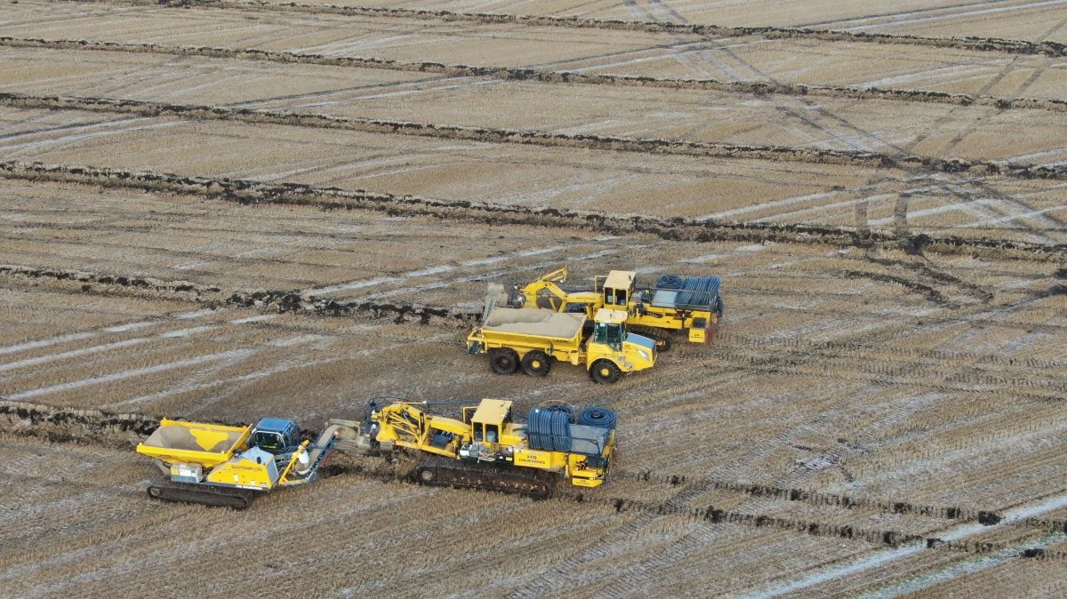 Øverst ses drænmaskine, og ved siden af den er en sand-dumper på hjul. Forrest nok en drænmaskine i arbejde, hvor den nye bæltedumper kører ved siden af.