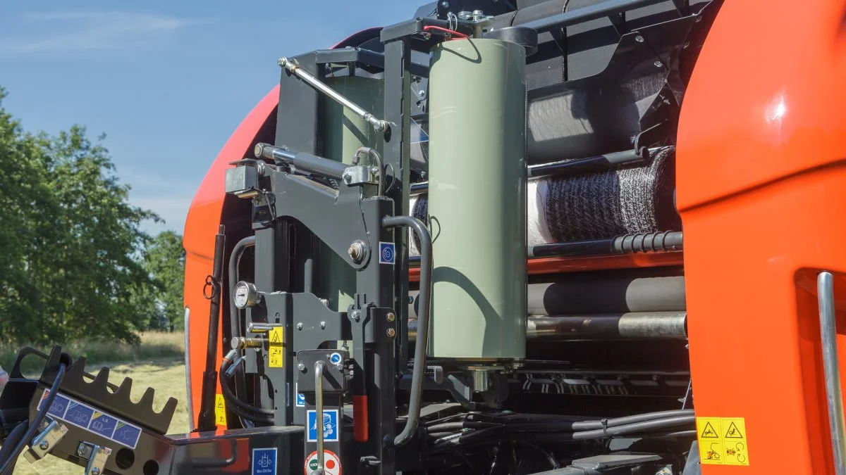 Bemærk de to standard wrapfilmruller, der leverer wrapfolien til selve bindingen og er helt samme type wrapfilm, som anvendes i wrapperen bag på maskinen. Inde bag skimtes en rulle til netbinding. Det er nemt at skifte mellem de to bindesystemer, og det sker uden brug af værktøj. 