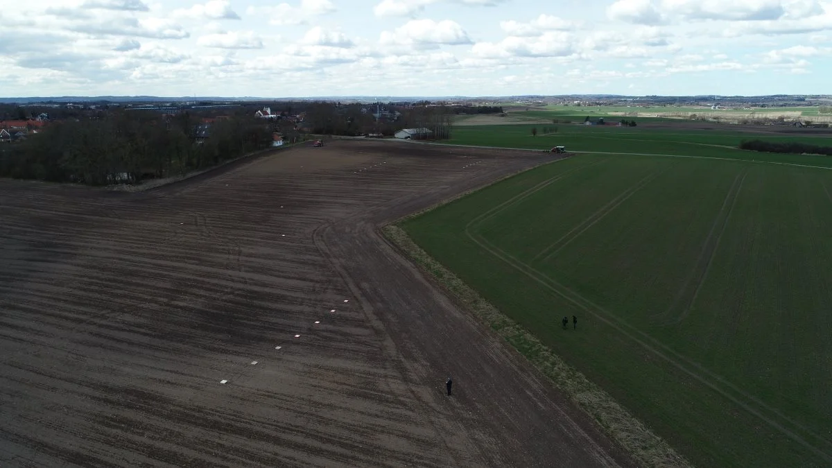 Landmanden kører med gødningsspreder i marken.