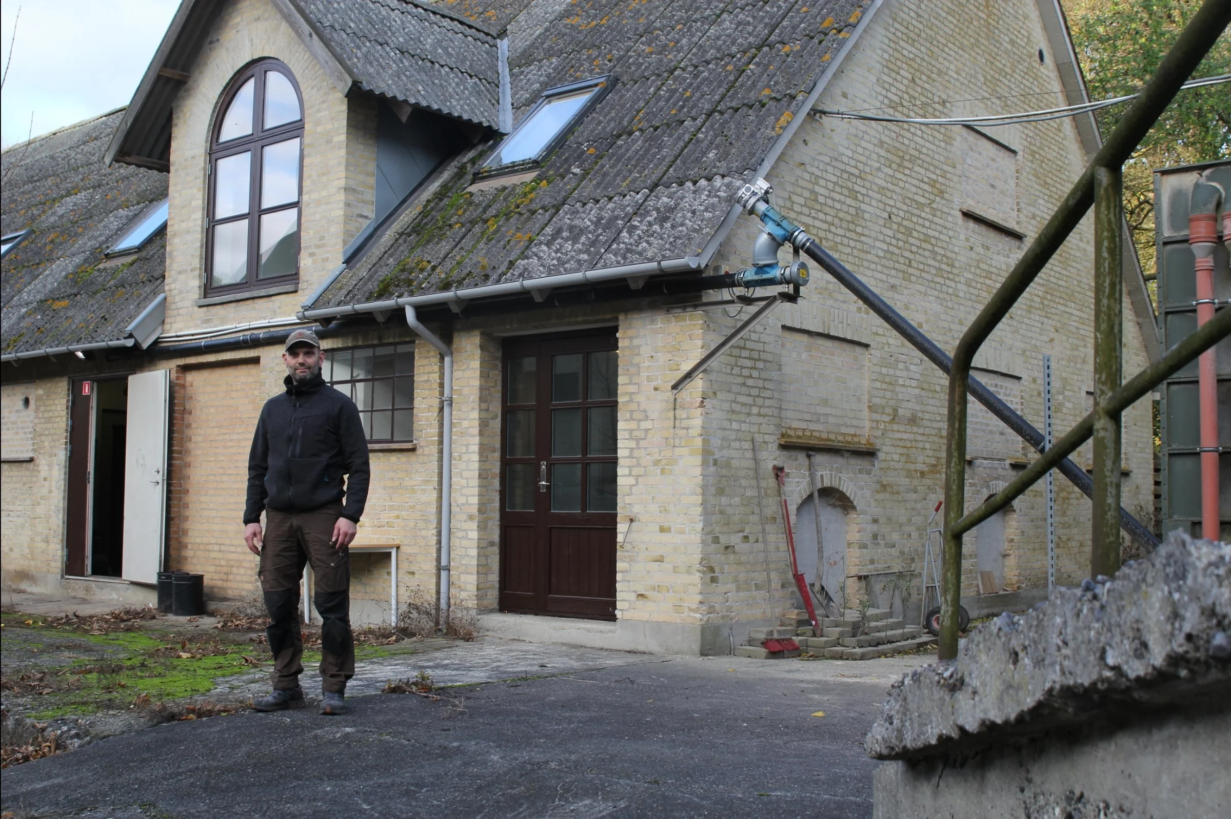 Pedel Kenneth Friis fortæller, hvordan træpillerne gennem rør op under taget kommer fra siloen, der skimtes yderst til højre, ind til fyret i rummet ved den åbne dør til venstre. Foto: Jesper Hallgren
