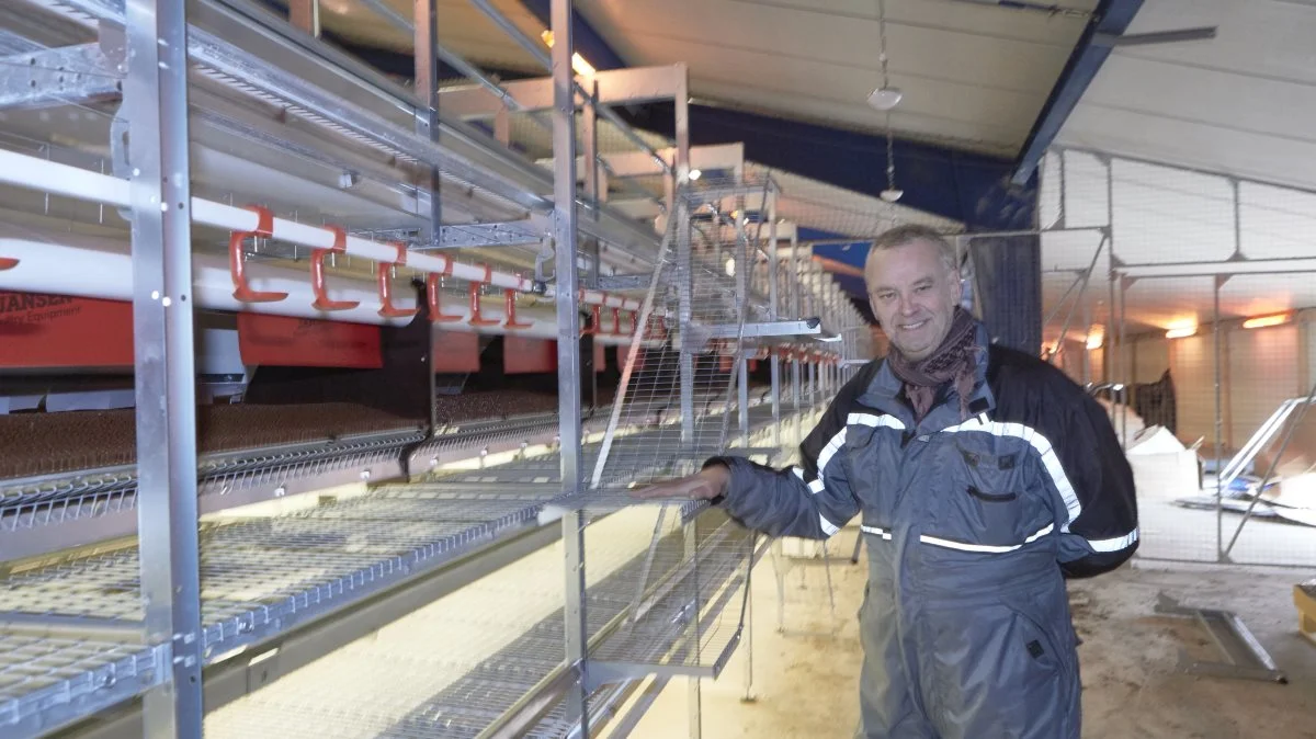 Michael Balle viser det næsten færdigmonterede staldanlæg. Via trappen eller ved selv at flyve derop, kan de økologiske høns benytte redekasser med den røde skærm, de røde vandnipler, foderbordene på alle tre etager eller pindene øverst til at overnatte på. Fotos: Erik Hansen