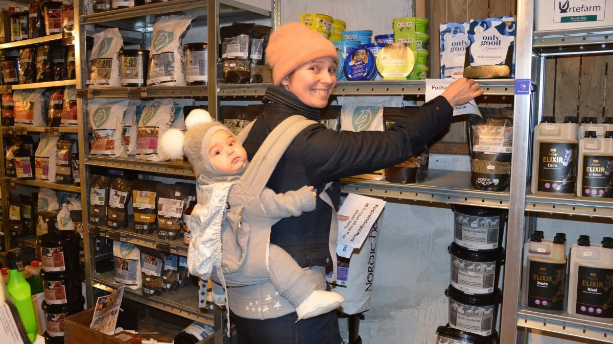 Med Bella på ryggen piller Maria Wichmann opslagene med fødselsdagstilbud af hylderne i butikken, der netop har fejret fire års fødselsdag. Fotos: Camilla Bønløkke