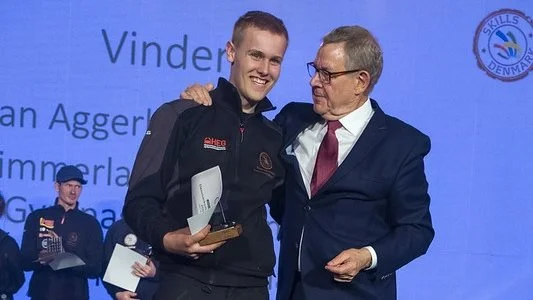 Poul Nyrup Rasmussen, tidligere statsminister og formand for EuroSkills 2025 overrakte trofæet til vinderen, Jan Aggerholm Andersen - Danmarks bedste entreprenørmaskinmekaniker.