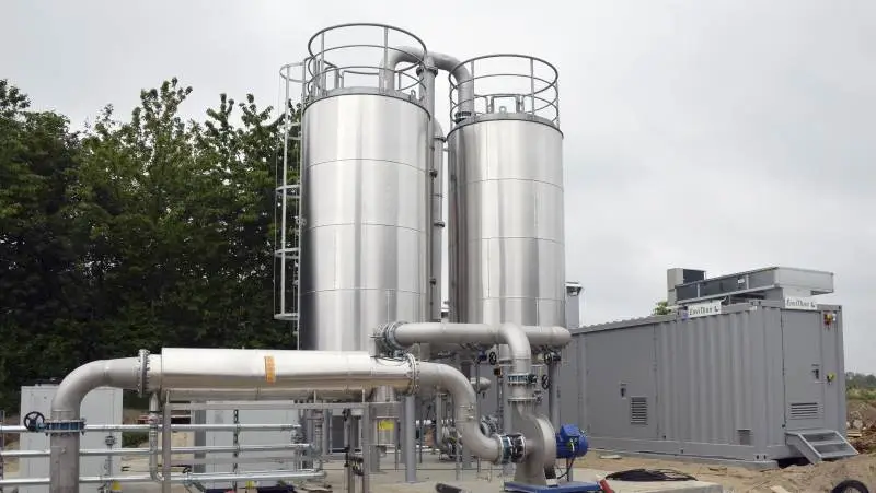 Inden Biogassen kommer ind i opgraderingsanlægget (den grå container) for at blive opgraderet til naturgas, renses den i kulfiltre i de to blanke ståltårne.